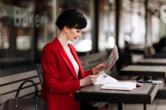 A attractive businesswoman in corporate outfit red blazer holding morning newspaper while sitting on