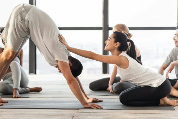 Female coach correcting yoga beginner at group class training in studio