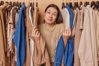 Hesitant woman shrugs shoulders feels unaware chooses perfect outfit for occasion wears knitted