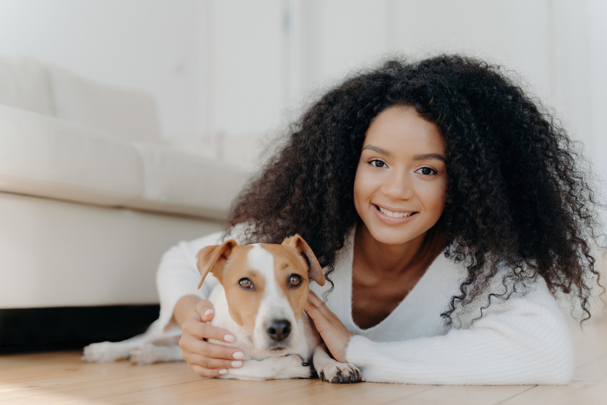 Pretty girl with Afro hair lies on living room floor, sharing pleasant emotions with newly adopted d